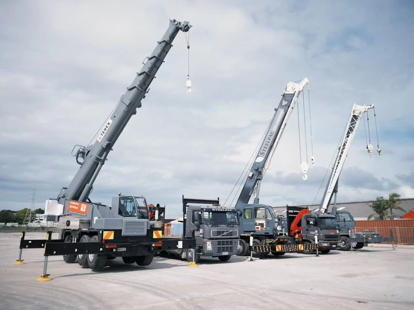 Steelpac's crane and truck fleet lined up in the Penrose yard, booms raised against an Auckland sky.