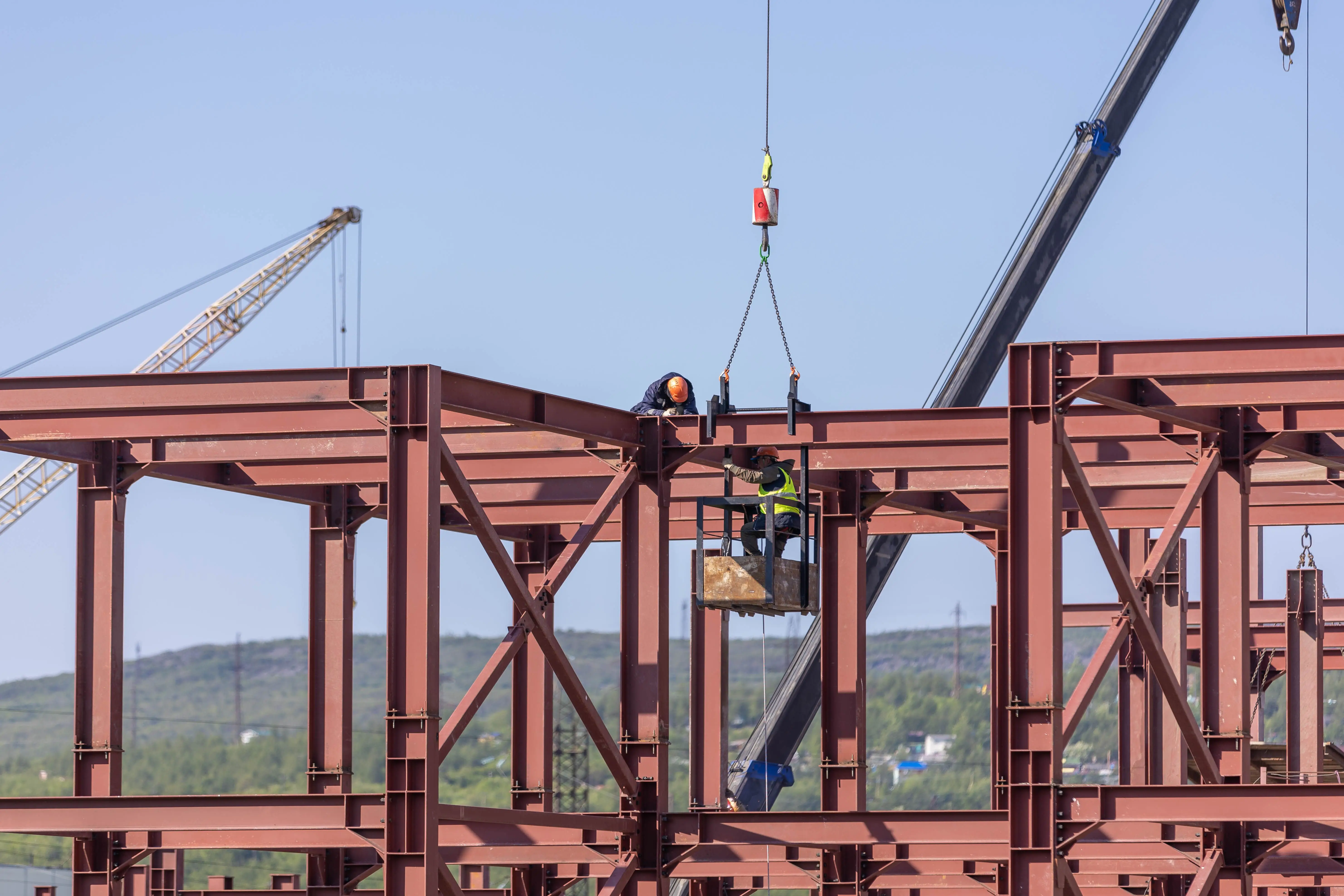 Workers installing a structural steel frame with cranes on a construction site.